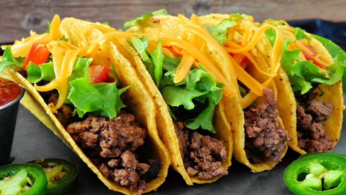 Group of hard shelled tacos with ground beef, lettuce, tomatoes and cheese close up