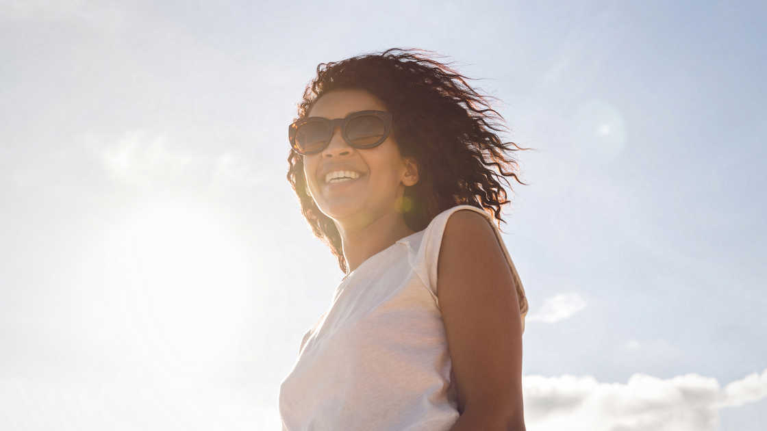 Woman with sunglasses standing in sunshine smiling